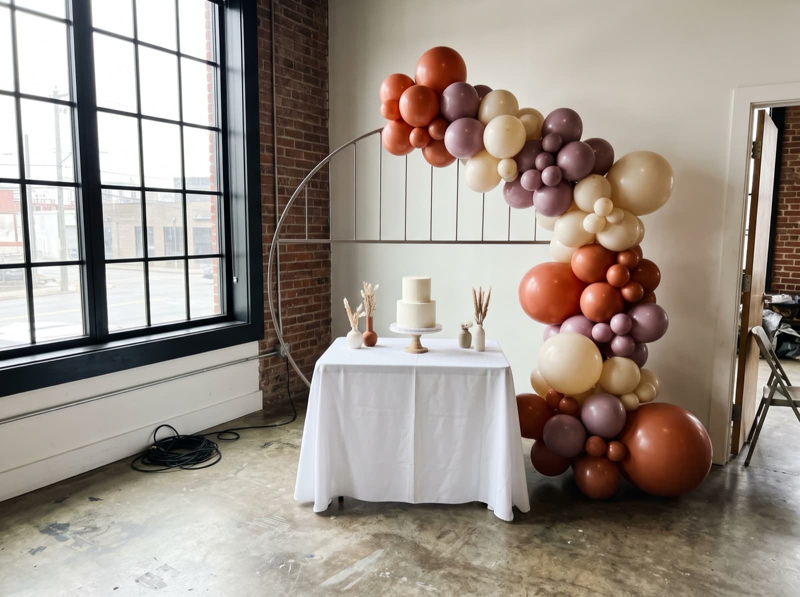 Half balloon arch in terracotta, mauve and cream over a cake table